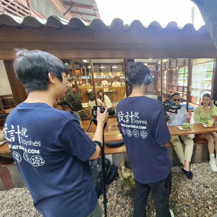 Crew filming two guests at the counter of an open-fronted wooden garden café